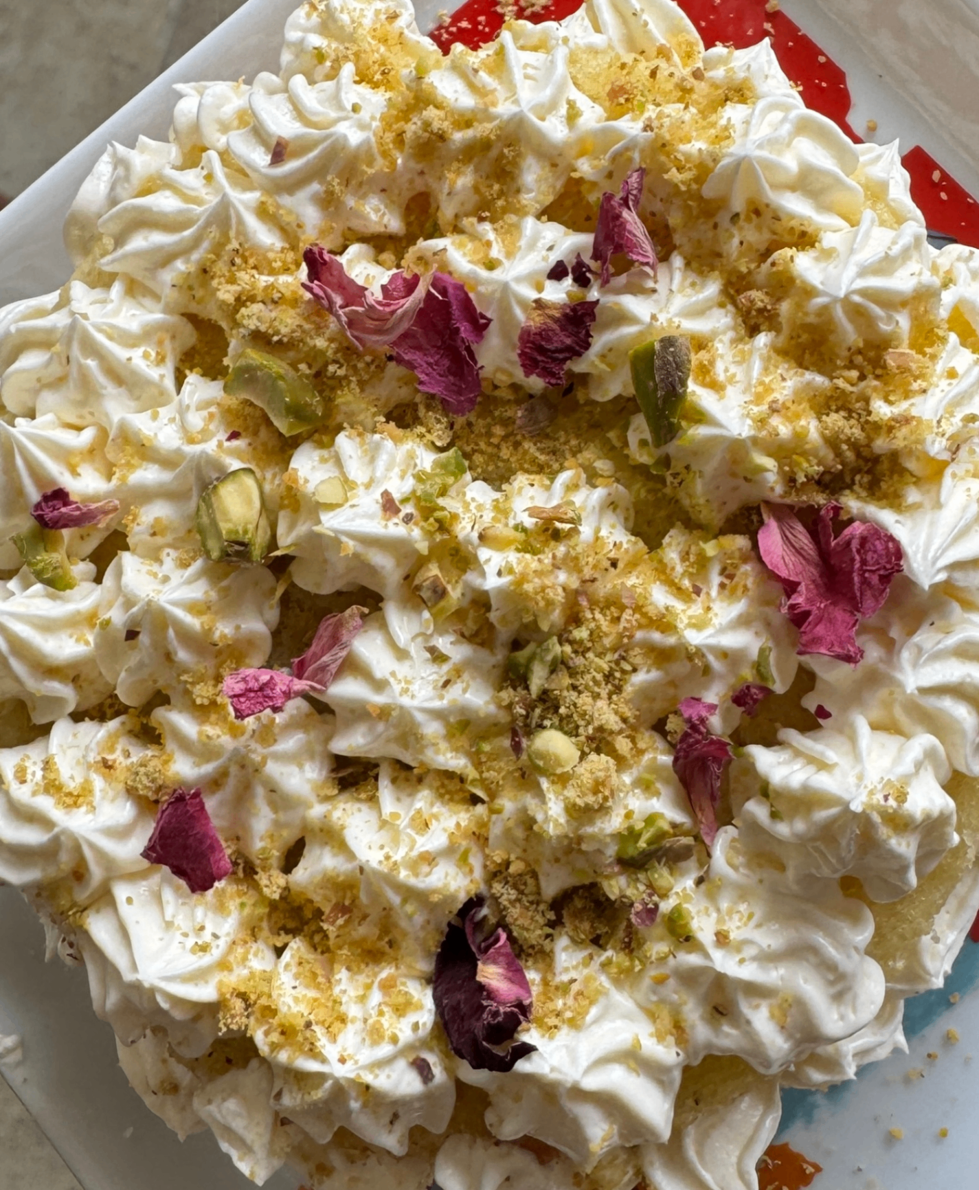 Cake topped with whipped cream, pistachio, and rose petals